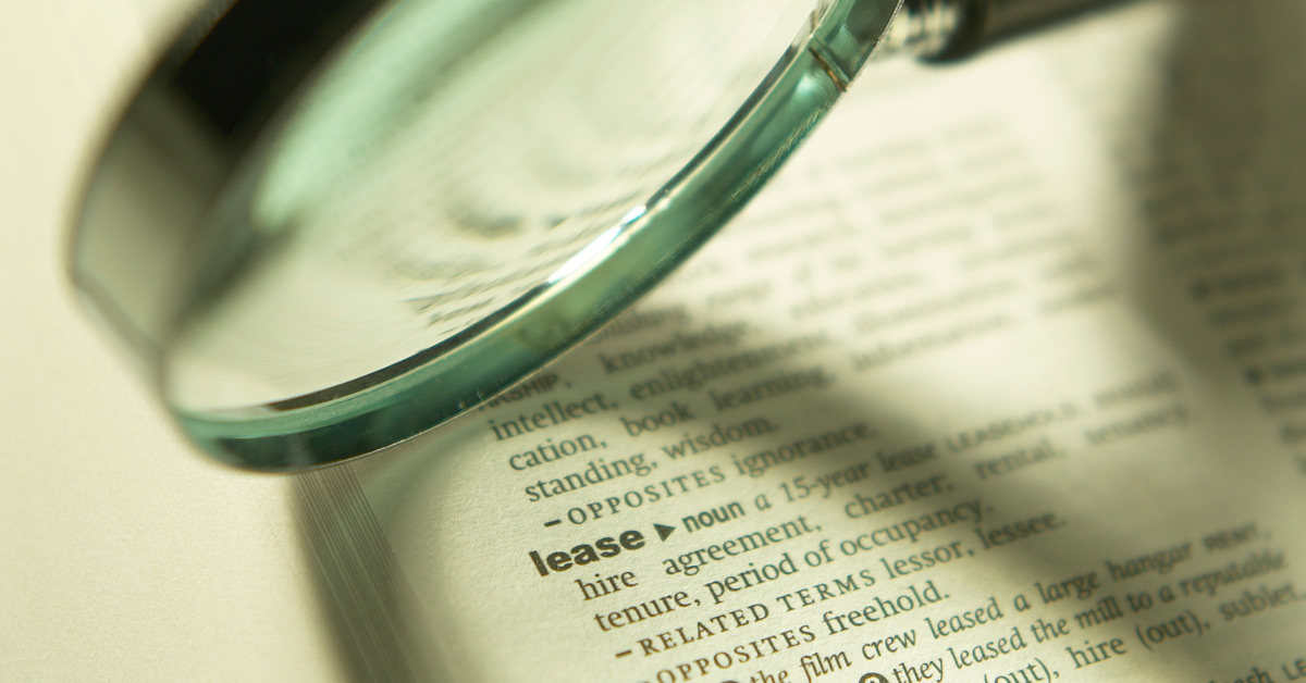 A magnifying glass enlarges the definition of "lease" on a dictionary page, highlighting words like agreement and tenure.