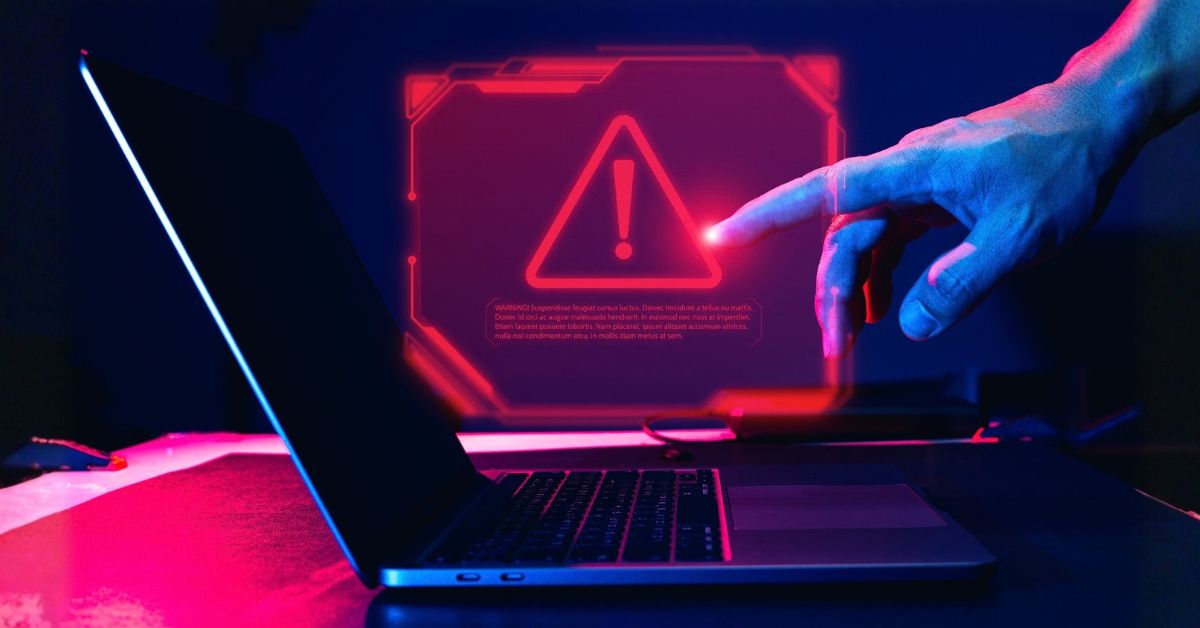 A hand points toward a glowing red warning symbol on a laptop screen, creating a dramatic cyber-security alert in neon blue and pink light.