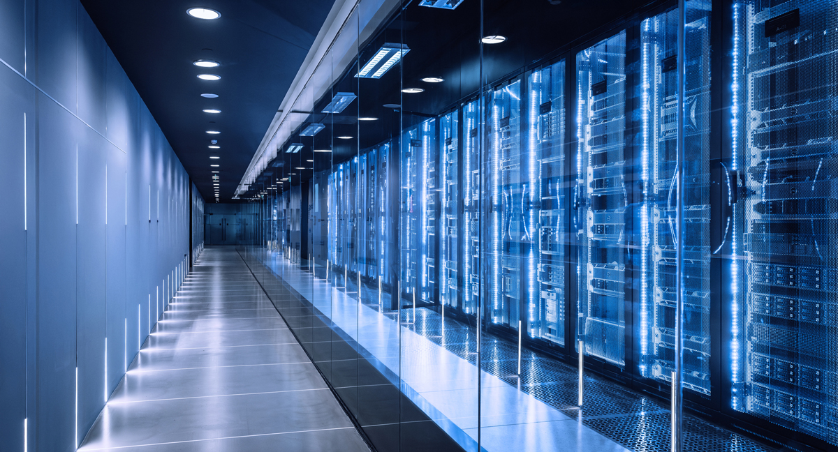 A long, empty data center corridor lined with glowing blue server racks behind glass, reflective floor, and cool lighting create a quiet, futuristic mood.
