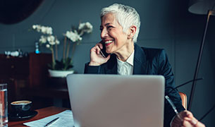 Image Businesswoman on a cell phone in front of a laptop sitting at the desk.