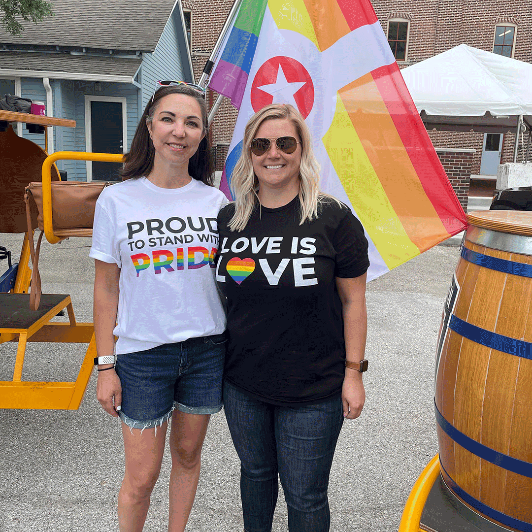Two Stewart employees wearing pride month shirts at a outdoor venue.