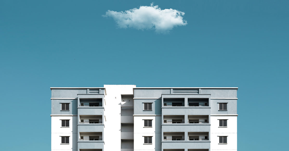 Image Top four floors of a condominium against a teal sky with single white cloud hovering above.
