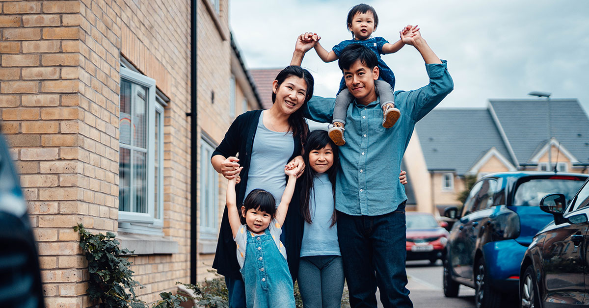 Image Asian American family of five pose together for a family photo on a sidewalk of a suburban neighborhood. 