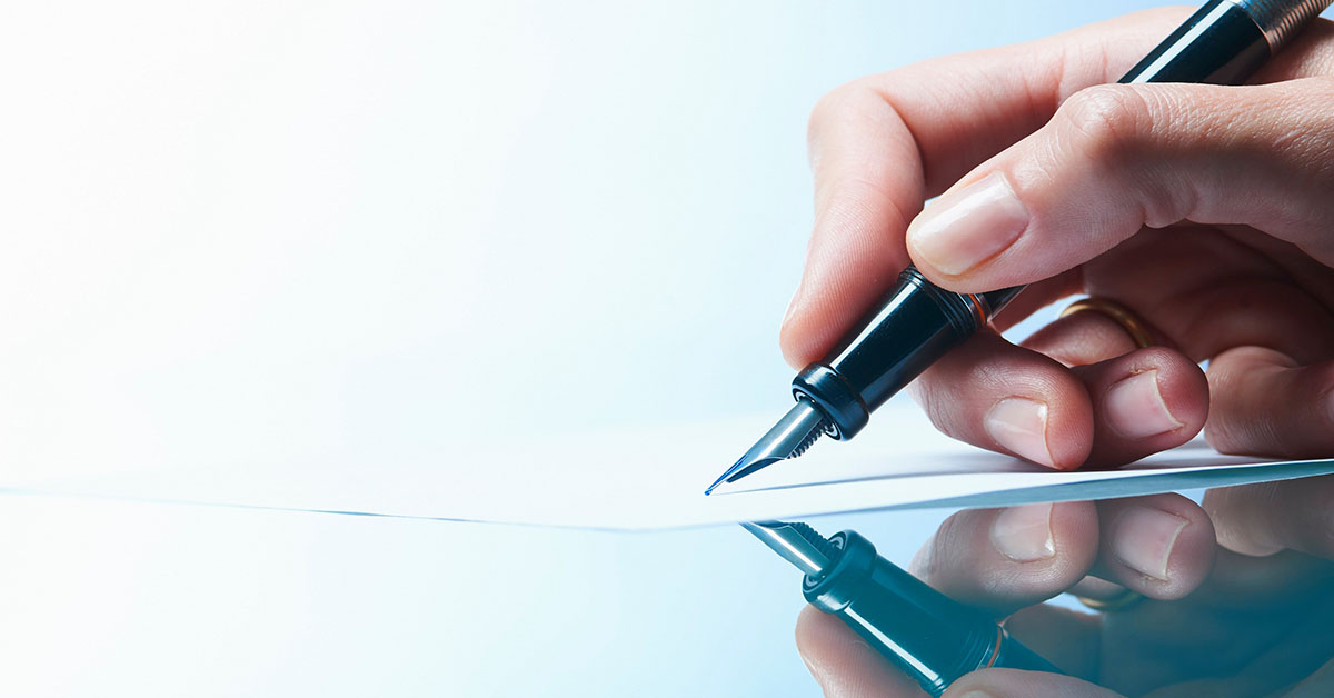 Image Close up of a woman's hand signing a document on a glass table with a fountain pen.