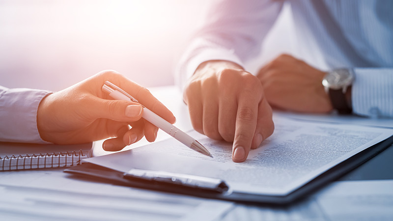 Image Hands of two different businessmen point at a contract from opposite sides of a table.