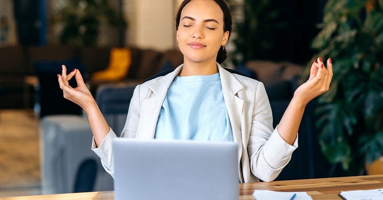 Young female meditates with eyes closed in front of a laptop.