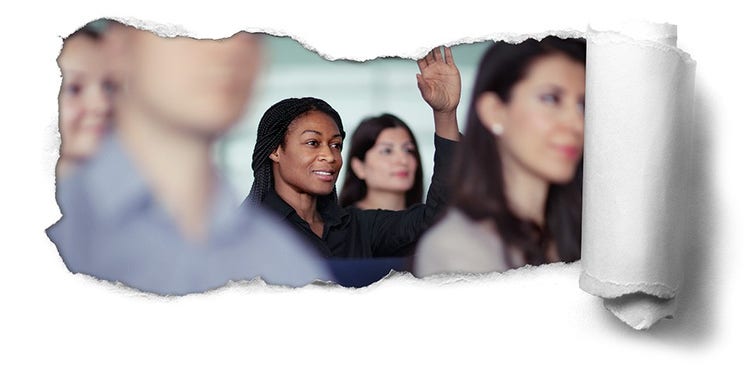 Business professional group in a classroom setting with focus on woman raising her hand.