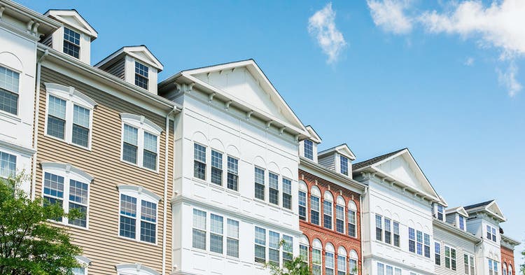 Row of modern apartment buildings showcasing varied architectural styles and colors under a bright blue sky with scattered clouds.