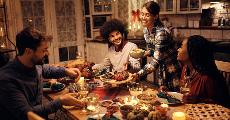 Happy woman brings food to the table while hosting Thanksgiving dinner
