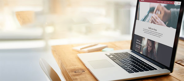 Laptop on wooden desk featuring the Stewart Now web portal.