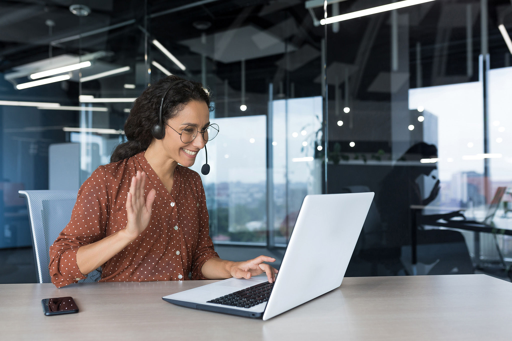 Young woman with curly hair wears headset on laptop video call